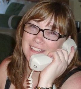 A close-up of Liz Pelletier smiling and holding a landline phone handset to her ear.