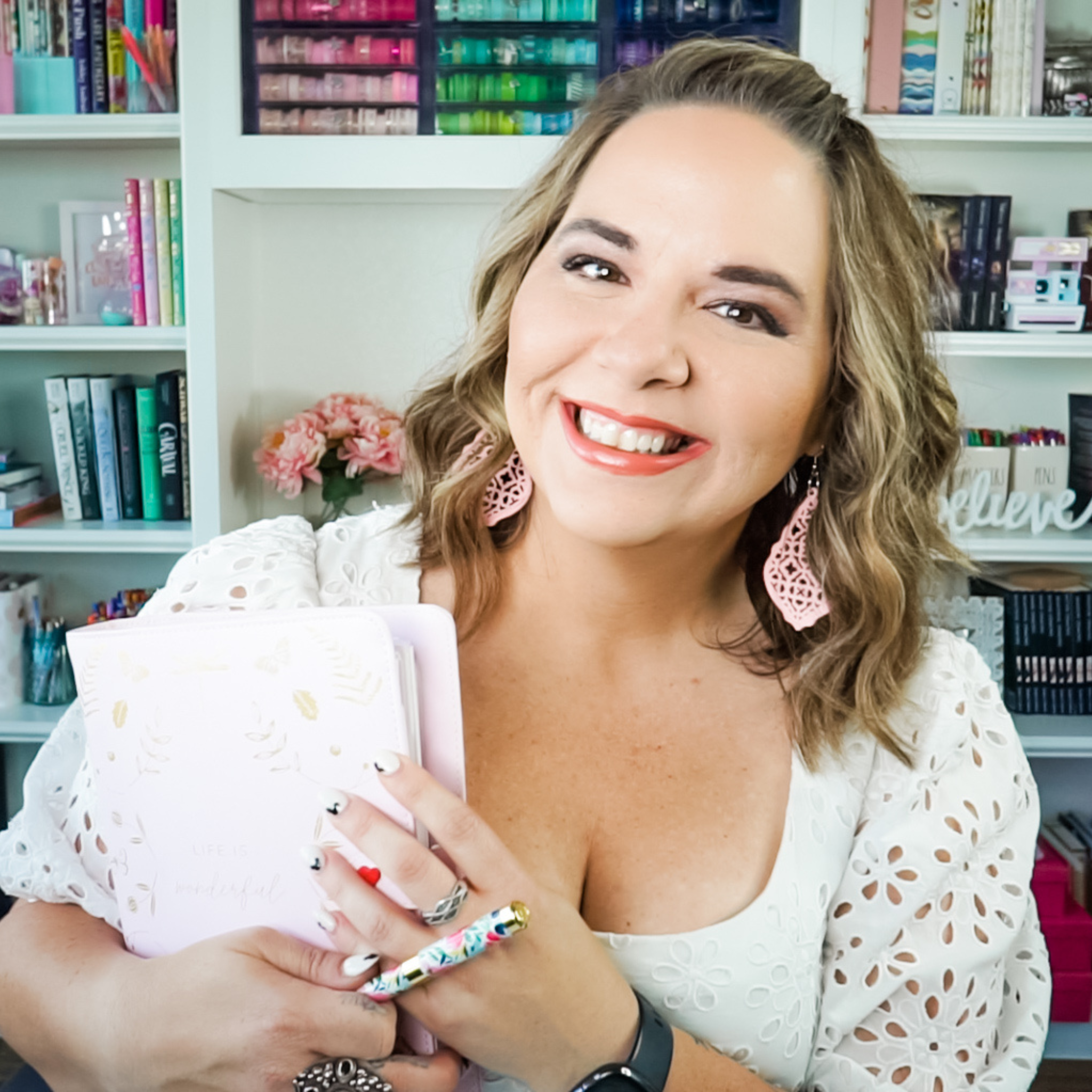 Sarra Cannon in front of a white bookshelf, smiling and holding a sheaf of papers and a pen.