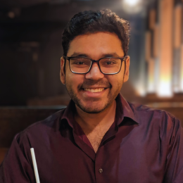 The smiling author wearing glasses and a purple button-up dress shirt