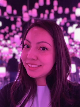 Pink-tinted close-up of the author, a woman with long brown hair, smiling in front of a blurry crowd background.