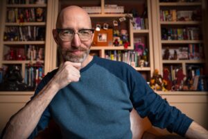 The author posed in front of a bookcase, with his right hand on his chin.